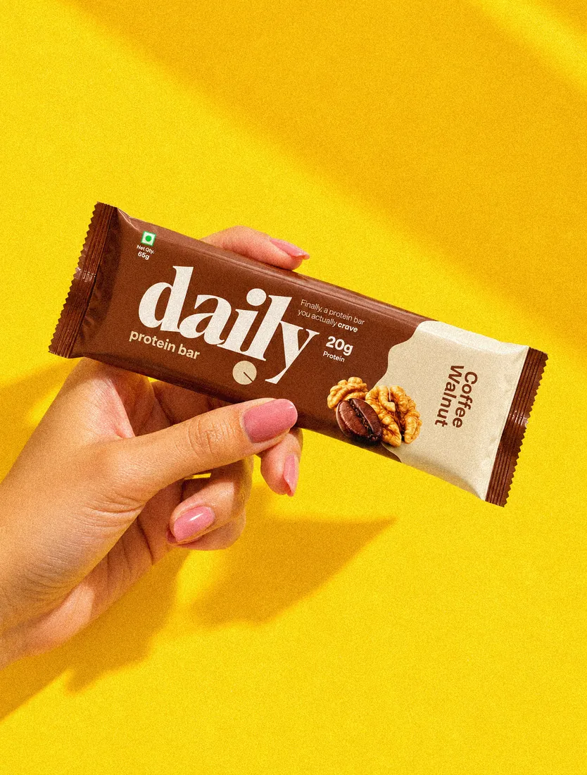 A hand holding a Coffee Walnut daily bar against a yellow background